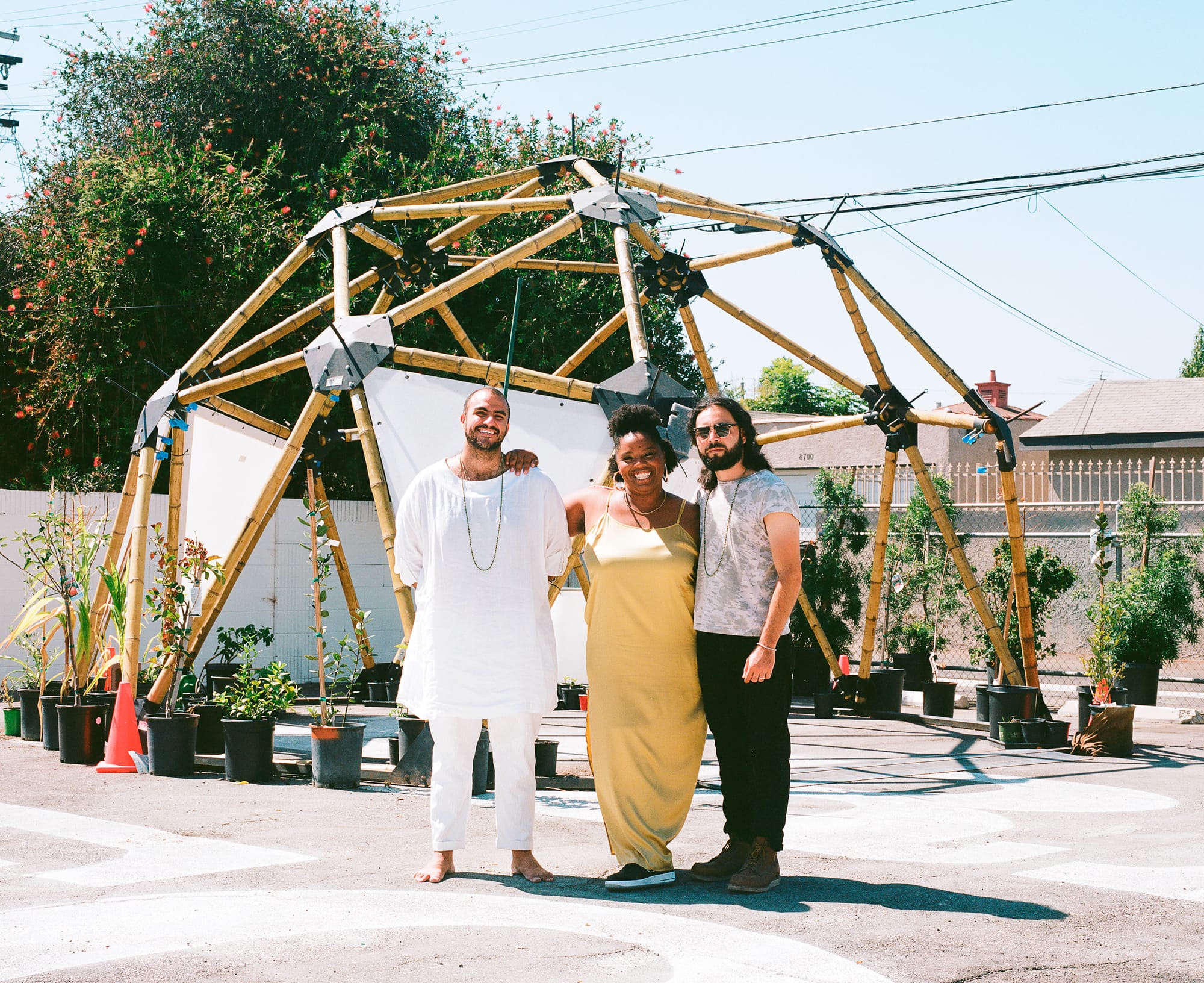 Three people stand in front of a geodesic dome outside