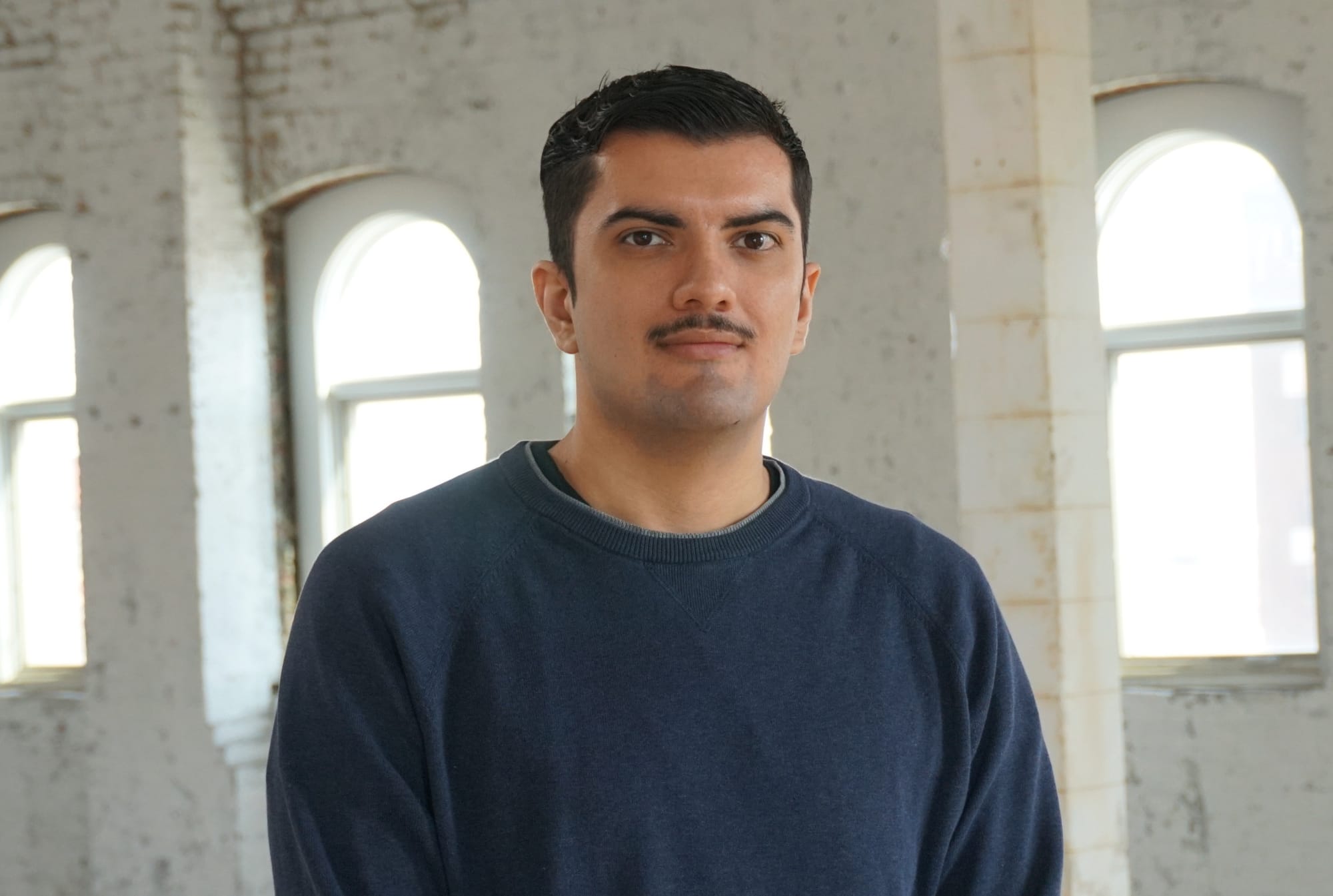 A young man with short black hair smiles in a warehouse space