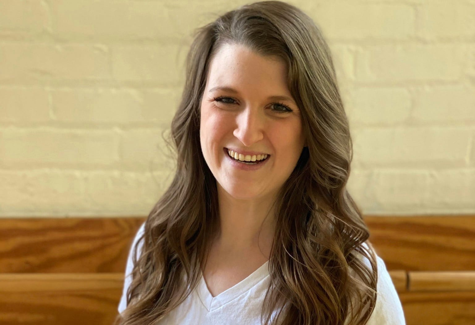 In a portrait, Stefany has long curly brown hair, a white t-shirt, and smiles