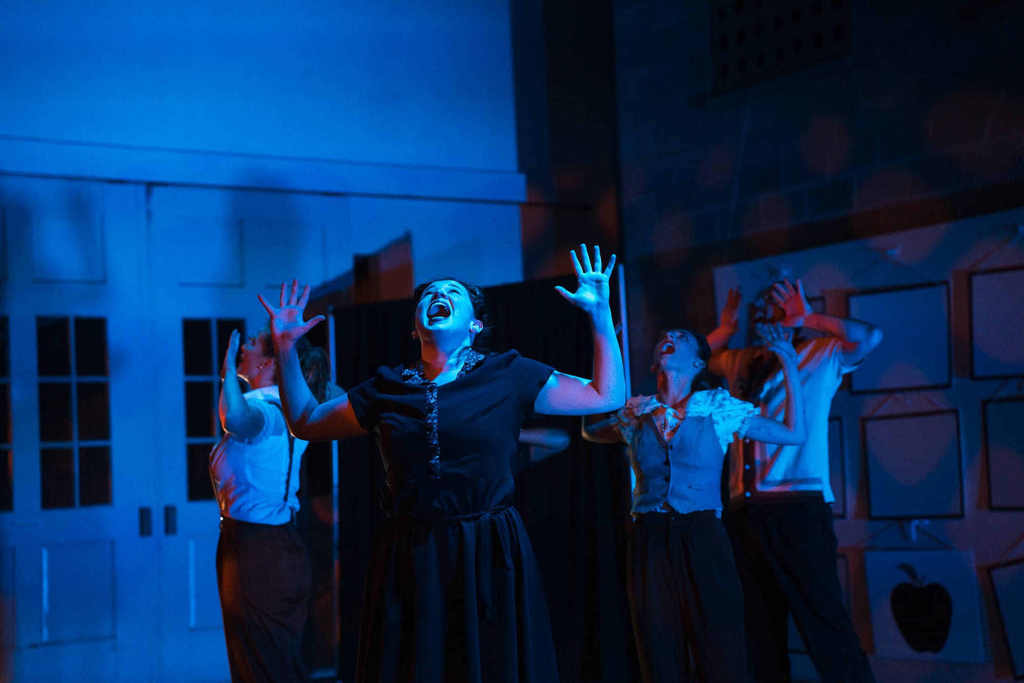 A moment on stage of Let the Record Show. Dancers hold their arms at right angles and open their mouths wide. 