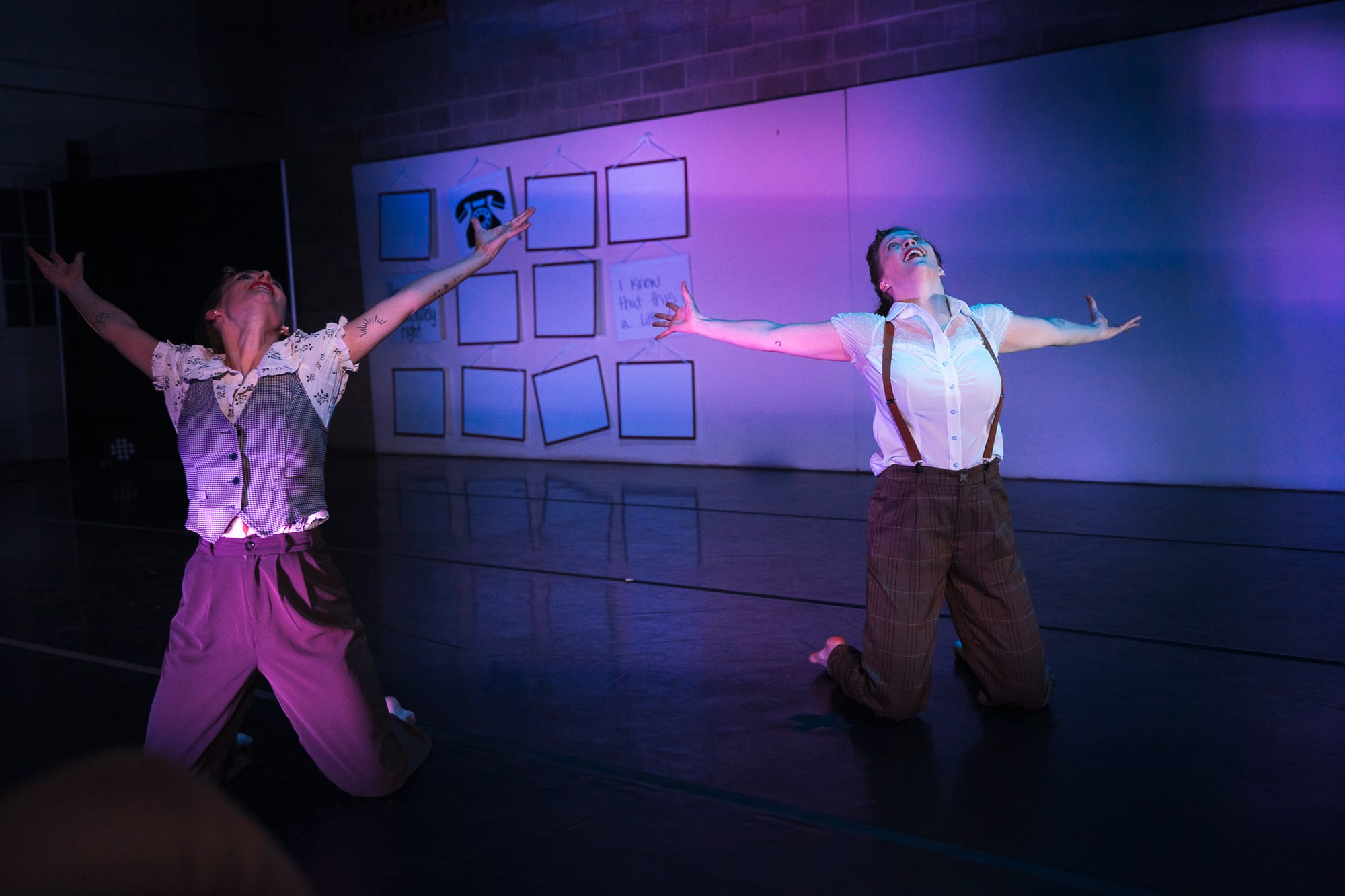 Two dancers kneel on stage in a joyous open-armed pose