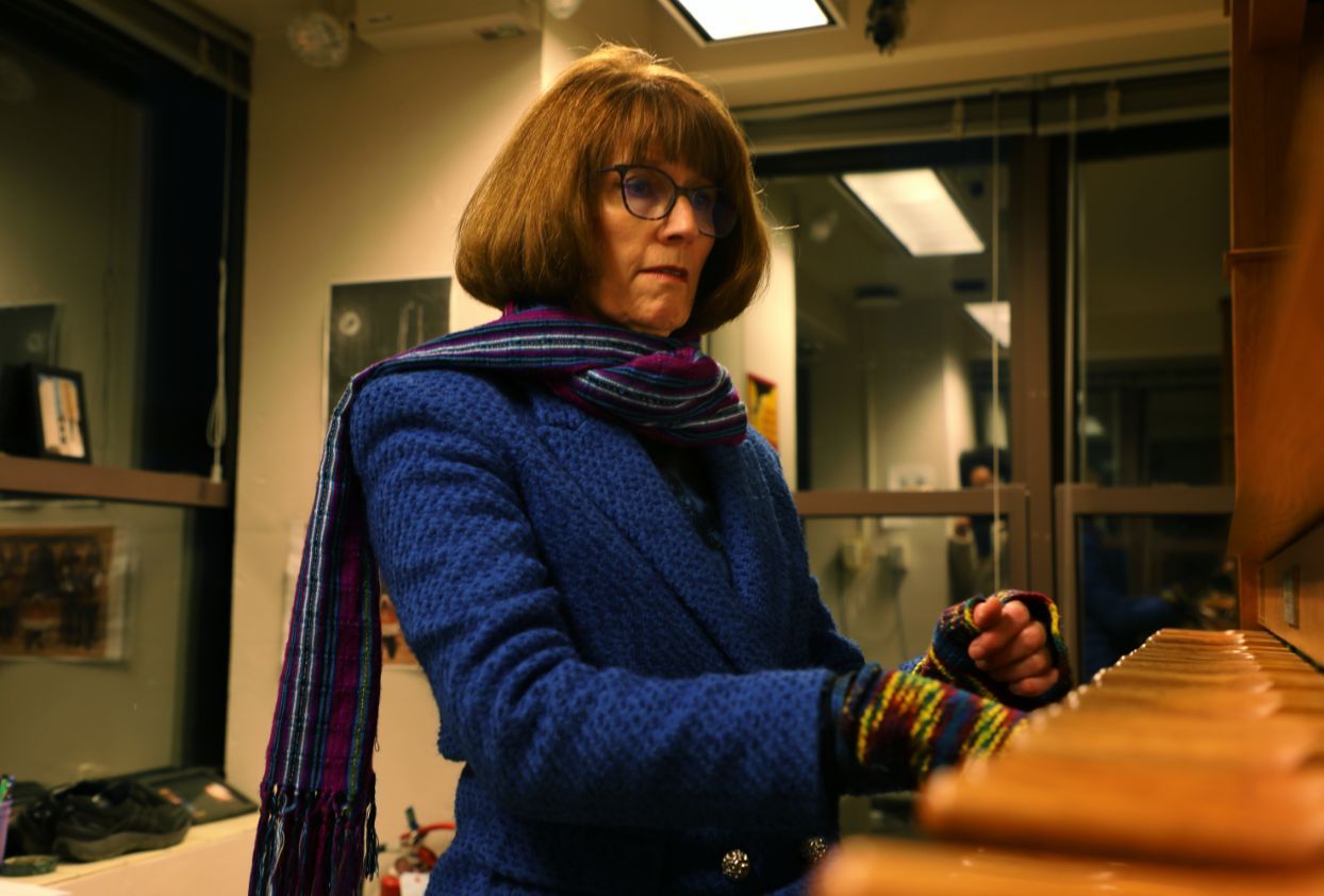 A-woman-with-short-blonde-hair-and-a-blue-blazer,-glasses-and-multicolor-gloves-plays-an-the-carillon.