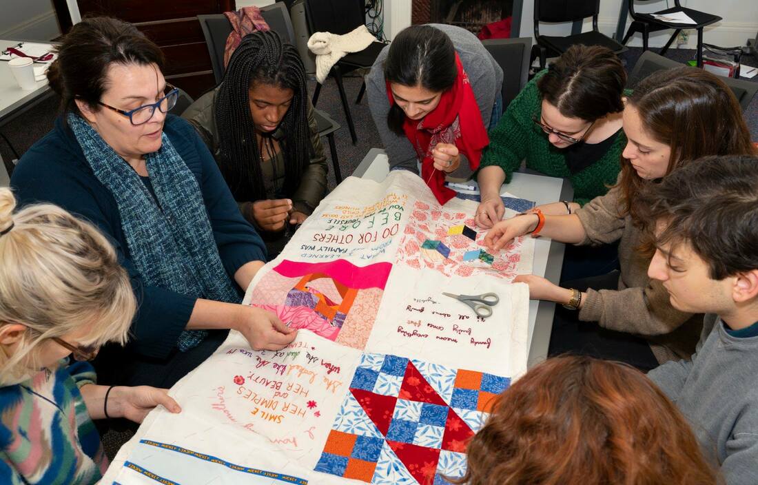 A-group-of-8-people-work-on-a-quilt-around-a-table.