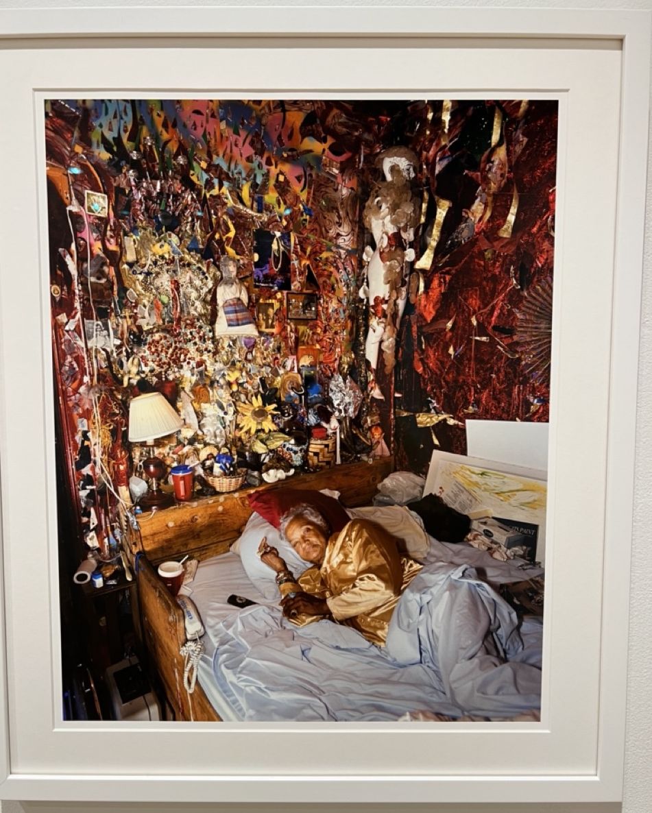 Artist dressed in silk-like pajamas lays in bed in her home art environment