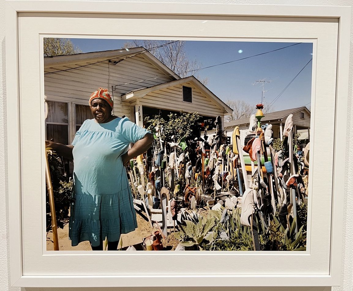 Image of a woman in a blue dress standing in front of her art work at home.